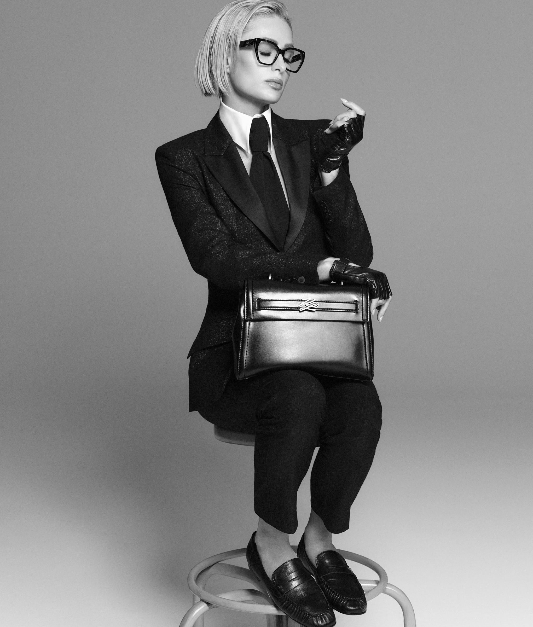 Person in a black suit holding a handbag on a gray background