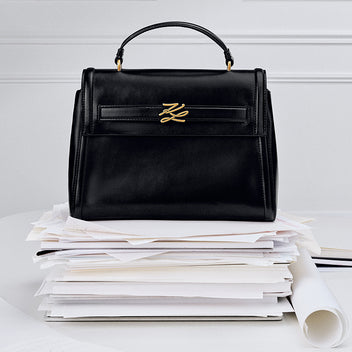 Black handbag with a gold logo on a stack of papers